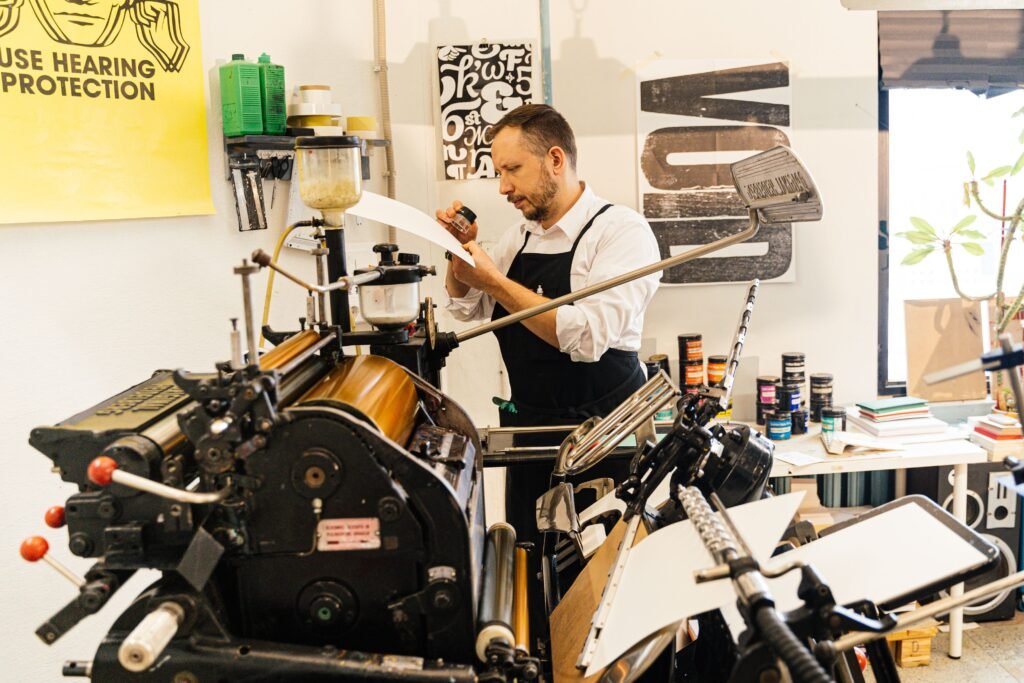 Man in apron working with vintage printing press in workshop setting, emphasizing craftsmanship.